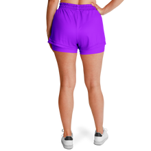 A woman shown from the back wearing neon purple athletic shorts and white sneakers against a plain white studio background.